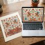 A printed folk-art illustration laid beside a laptop showing the same digital art file