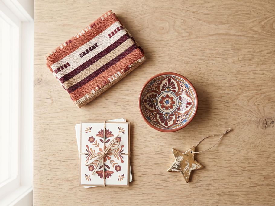 A styled flat lay of curated Folk Art Mexico pieces — woven textile, ceramic bowl, and art cards — in warm terracotta and cream tones