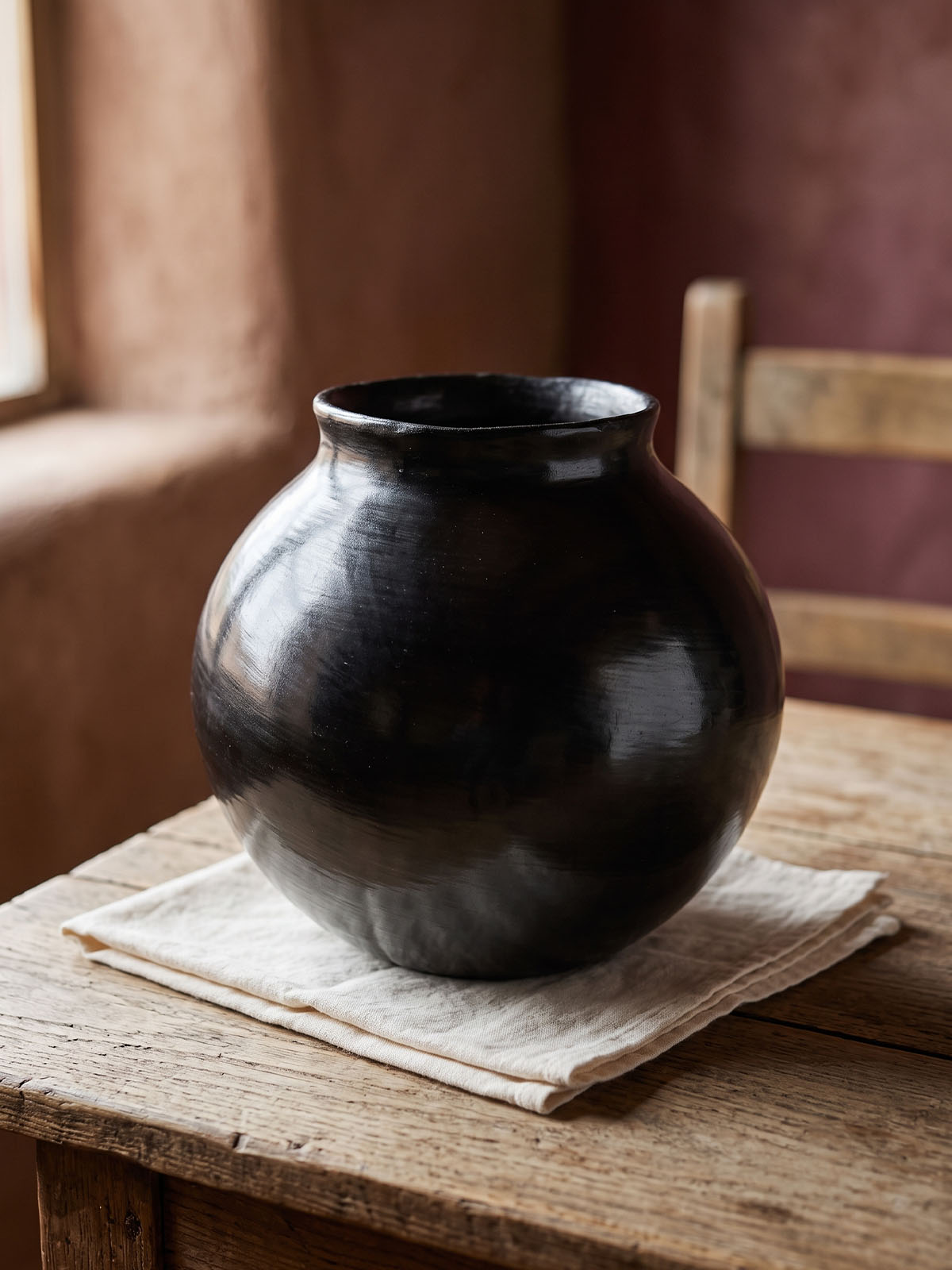 A finished black clay vessel catching natural light, showing the subtle unevenness of its hand-burnished surface