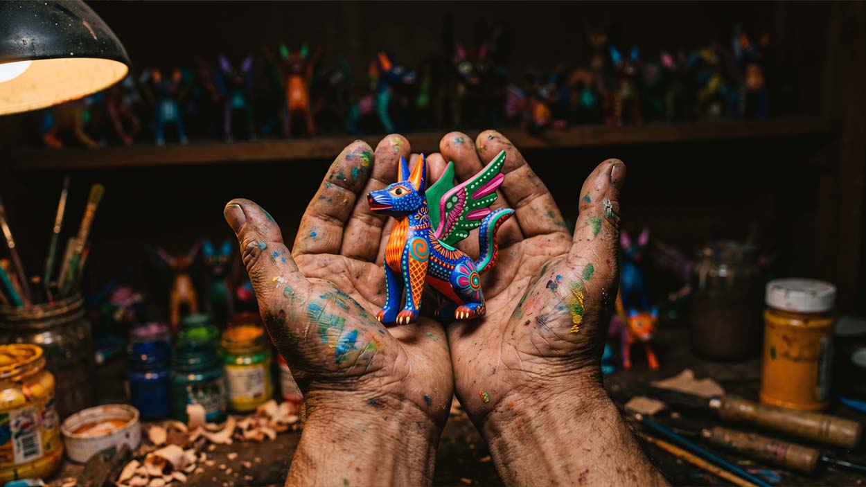 Artisan hands cradling a finished Alebrije figure in a dim Oaxacan workshop