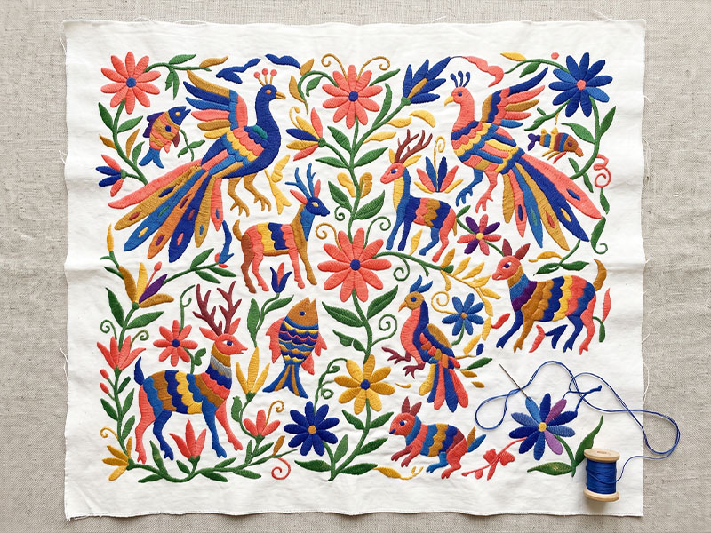 Close-up of Otomí embroidery showing bold animal and floral motifs in bright thread on white cotton cloth, Hidalgo