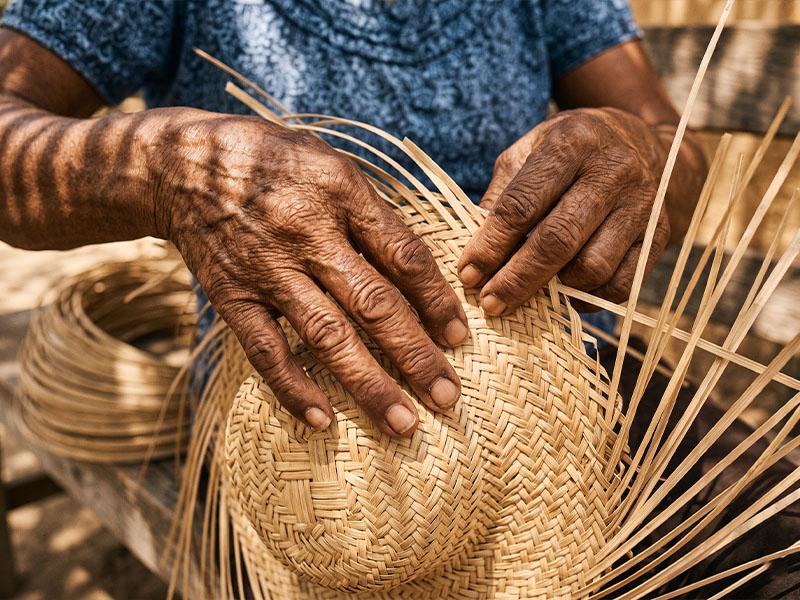 Artisan plaiting dried palm strips into a sombrero in a coastal Guerrero community, hands working without looking down