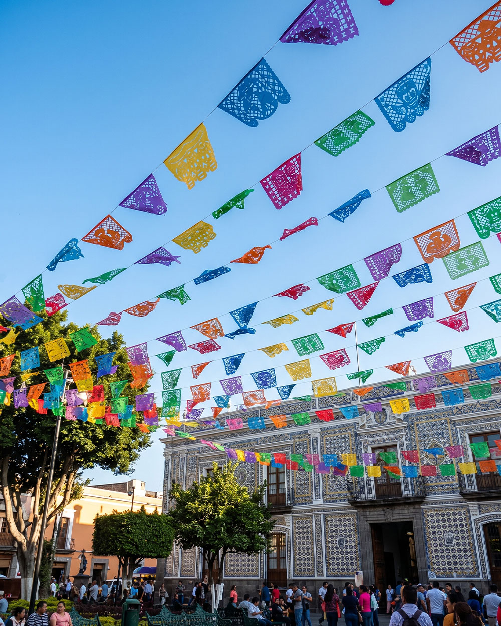Papel picado banners over a Puebla plaza with a Talavera-tiled facade